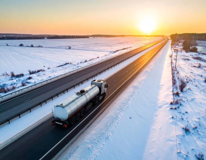 Petrol cargo truck lorry tanker driving on highway hauling oil products at sunrise, wide snowy
