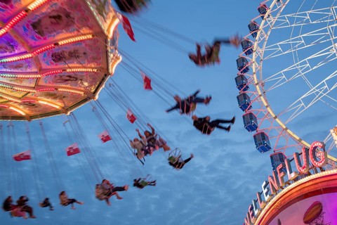 An illuminated chain carousel turns at night at a funfair, with floating people and colourful
