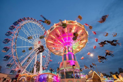 An illuminated chain carousel and Ferris wheel at night at a funfair, people swinging on chains,