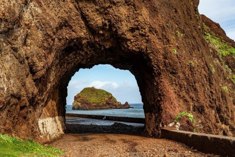 View of the small island of Ilhéu da Ribeira da Janela, Madeira, Portugal, through a tunnel carved
