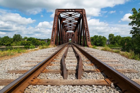 Railroad tracks leading to old rusted Terrebonne Pratt truss railroad bridge over Des Mille-Iles