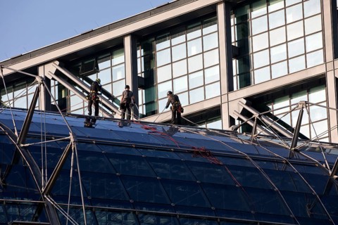 Three male glass cleaners abseiling down a glass roof of Berlin Central Station to clean windows,