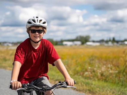 A boy with a bicycle helmet rides a bicycle and smiles friendly into the camera, AI generated, AI