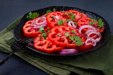Freshly sliced tomatoes and red onions, garnished with herbs, on a black plate, summer salad, no