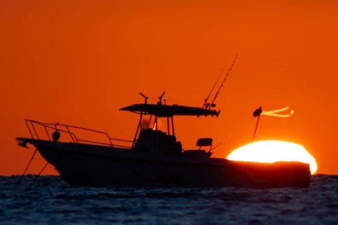 The sun rises behind a boat on the Costa Rei, a coastal stretch of the Italian Mediterranean island
