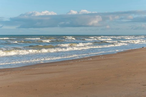 The waves crash gently against a rocky shoreline at sunset, creating a tranquil atmosphere. The
