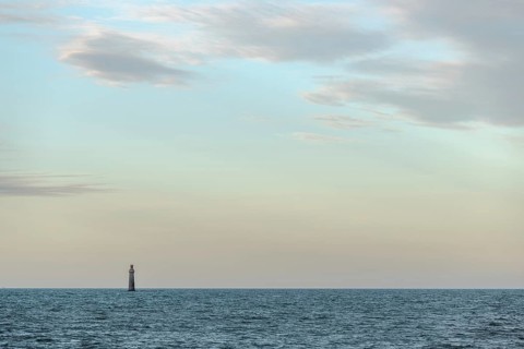 A lighthouse rises from the gentle waves of the ocean, surrounded by a tranquil seascape. Soft