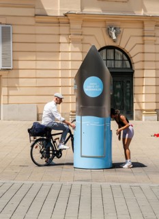Two people in front of a drinking water fountain in the city centre of Vienna, Austria