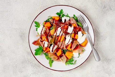 Salad with slices of ripe melon, prosciutto, mozzarella and fresh arugula, decorated with balsamic