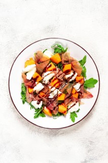 Salad with slices of ripe melon, prosciutto, mozzarella and fresh arugula, decorated with balsamic
