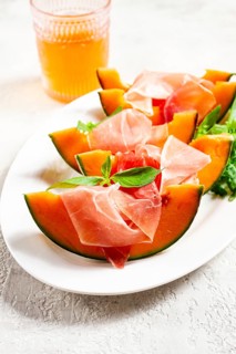 Cantaloupe melon with prosciutto and fresh basil, on a white plate, natural light