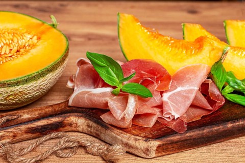 Cantaloupe melon, with prosciutto, and fresh basil, on a wooden serving board, rustic style