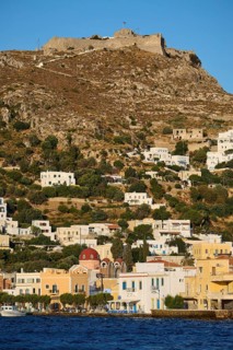 Panteli Fortress, White houses stretch along a hill with a fortress at the top and the sea in the