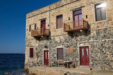 Stone house with red windows and balconies right on the waterfront in sunny weather, Agia Marina,