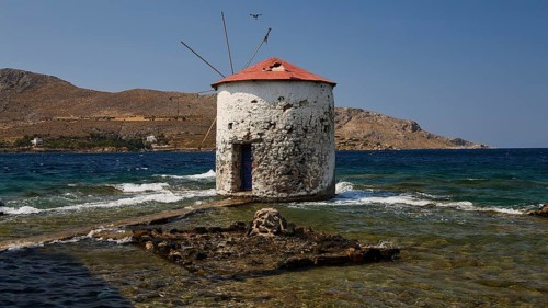 Old windmill in the middle of the sea, surrounded by foaming waves and a deep blue sky, Agia