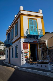 Corner building in white and yellow with blue shutters, souvenir shop on a sunny street, Agia