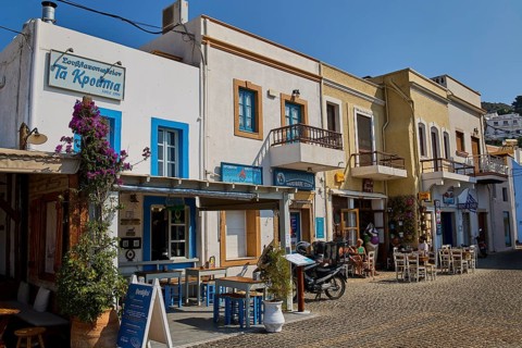 Row of historic buildings with restaurants and flowers on cobblestone street in sunshine, Agia