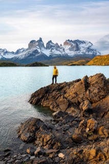 Young man on the shore of the blue lake Lago Pehoe in the evening light, Cuernos del Paine mountain