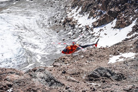 Red helicopter flies over glaciers in the mountains, Stubai Alps, South Tyrol, Italy