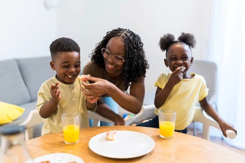 Mother joyfully feeding her children during a cozy breakfast at home, creating a warm atmosphere