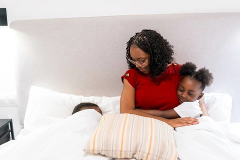 Young mother embracing her daughter in bed, while her son peacefully sleeping beside them, creating