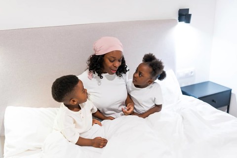 Mother undergoing cancer treatment, wearing a headscarf, sharing a heartwarming moment with her two