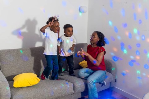 Mother and her two children enjoying dancing together in the living room, illuminated by colorful