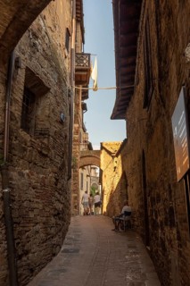 Alley in San Gimignano with historic walls, laundry in the wind and an elderly man on a chair, San