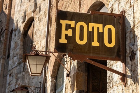 PHOTO sign in gold lettering hangs on a rustic stone wall in San Gimignano, Tuscany, Italy