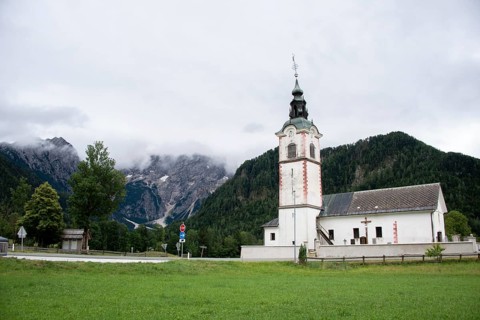White church building against a mountainous background under a cloudy sky, Zgornje Jezersko,
