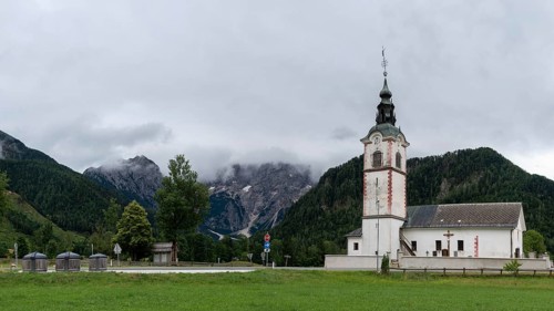 Church tower with red details in front of a mountainous landscape, Zgornje Jezersko, Gorenjska,