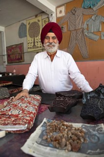 Indian Sikh, 68 years old, in his shop, in front bales of cloth and wooden panels for wood panel