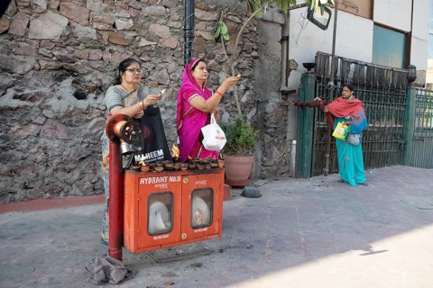 Indian woman holding tea lights in the air at a fire hydrant, Govind Dev Ji Hindu temple in the old