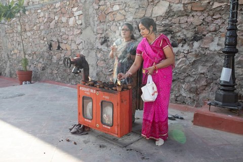 Indian woman lighting tea lights at a fire hydrant, Govind Dev Ji Hindu temple in the old city