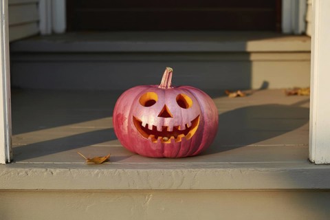 Pink spray-painted Halloween pumpkin with carved face on front porch. Unconventional seasonal