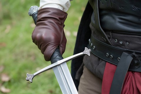 Close up of hand in leather glove holding medieval sword hilt with gemstone. Concept of medieval or