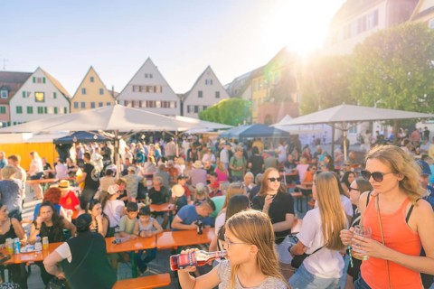 Visitors relax at tables in sunny weather, surrounded by historic house facades, 950 years Weil der