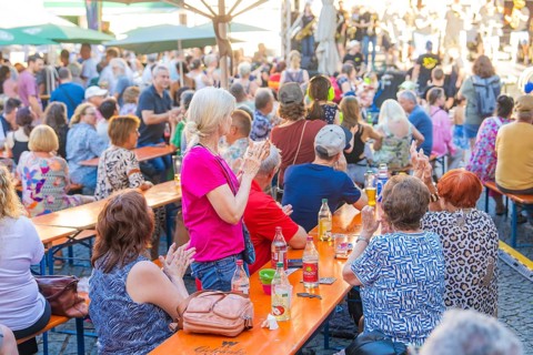 People sitting at long tables at a party, applauding and enjoying drinks, 950 years Weil der Stadt