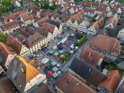 Lively town festival with numerous visitors and green trees surrounded by buildings seen from the