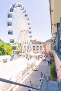 Ferris wheel next to a building with many people on a sunny promenade, Calw, Germany