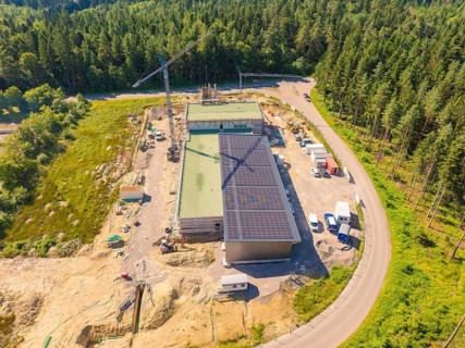 Aerial view of a construction site with solar panels, surrounded by woodland and a crane, new fire