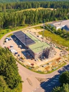 Building complex under construction near the forest, with solar panels and a crane visible, new