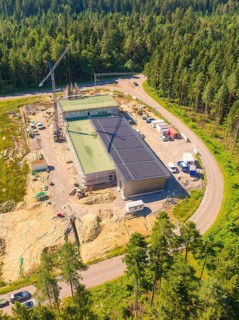 Building with solar roof in a construction site surrounded by forest, crane nearby, various