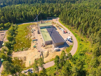 Solar roof building on a construction site surrounded by trees, crane and vehicles visible, aerial
