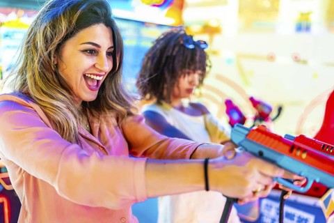 Two young women enjoying their summer vacation, playing arcade shooting games and having fun