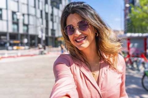 Smiling young woman wearing trendy sunglasses, capturing a joyful selfie in a vibrant city center