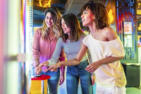 Three female friends enjoying a vibrant summer night out in the city, laughing and playing arcade