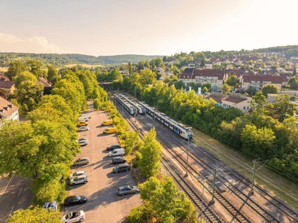 Train and cars in a green environment next to a housing estate, bright summer atmosphere, Weil der