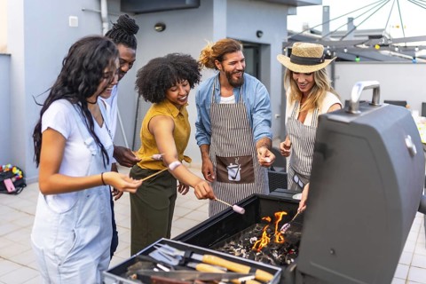 Happy friends enjoying a rooftop party, roasting marshmallows over a barbecue grill while sharing