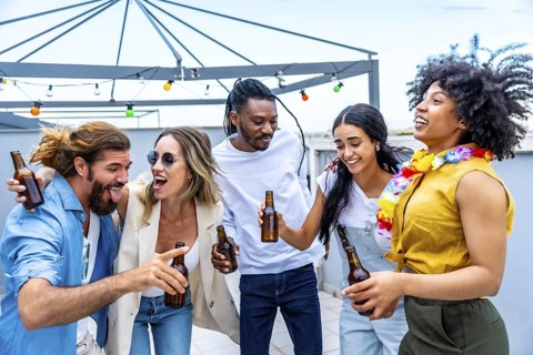 Cheerful multi ethnic friends laughing and enjoying drinks while celebrating together at a lively